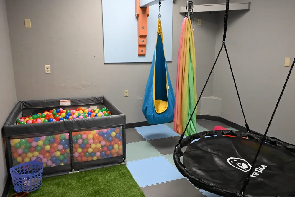 A calm corner with a ball pit, pod swing, and rainbow fabric hammock over soft turf