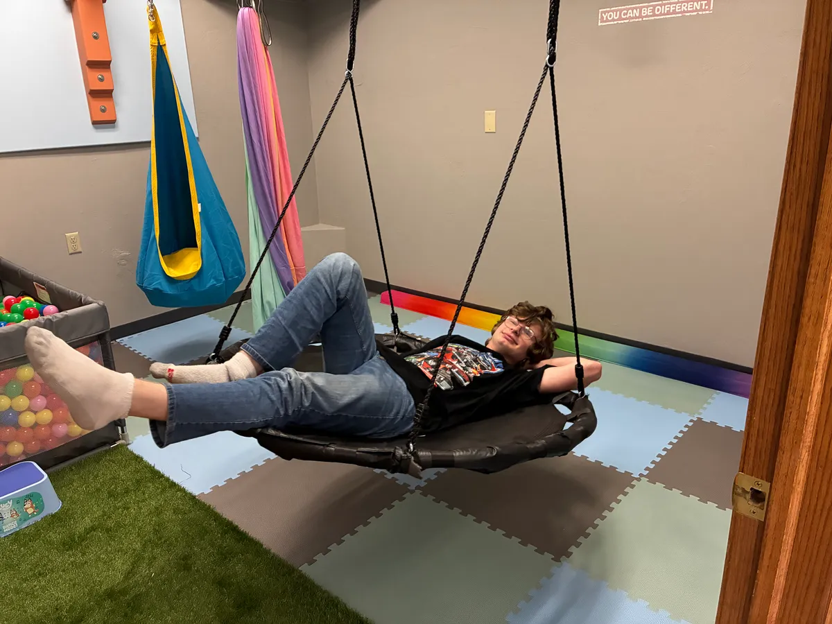 A teen lying back on a platform swing beneath a wall decal that reads “You can be different.”